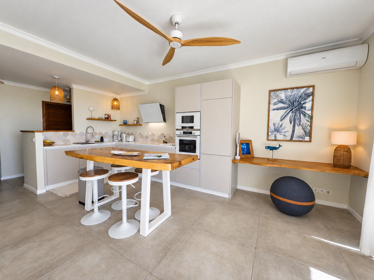 A modern kitchen with a central island, bar stools, a ceiling fan, and a wall-mounted air conditioner.