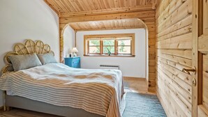 A cozy bedroom with a wooden ceiling, a bed with striped bedding, a bedside table with a lamp, and a window with a view of greenery. - 3 bedroom beautiful home in Melby (Melby)
