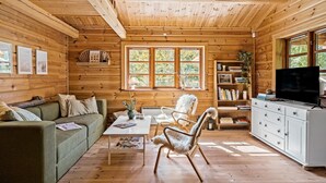 A cozy cabin interior with a wooden interior, a sofa, a coffee table, a chair, a bookshelf, and a television. - 3 bedroom beautiful home in Melby (Melby)