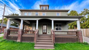 Ein zweigeschossiges Haus mit einer Veranda, einem kleinen Hauseingang und einem Vorgarten.