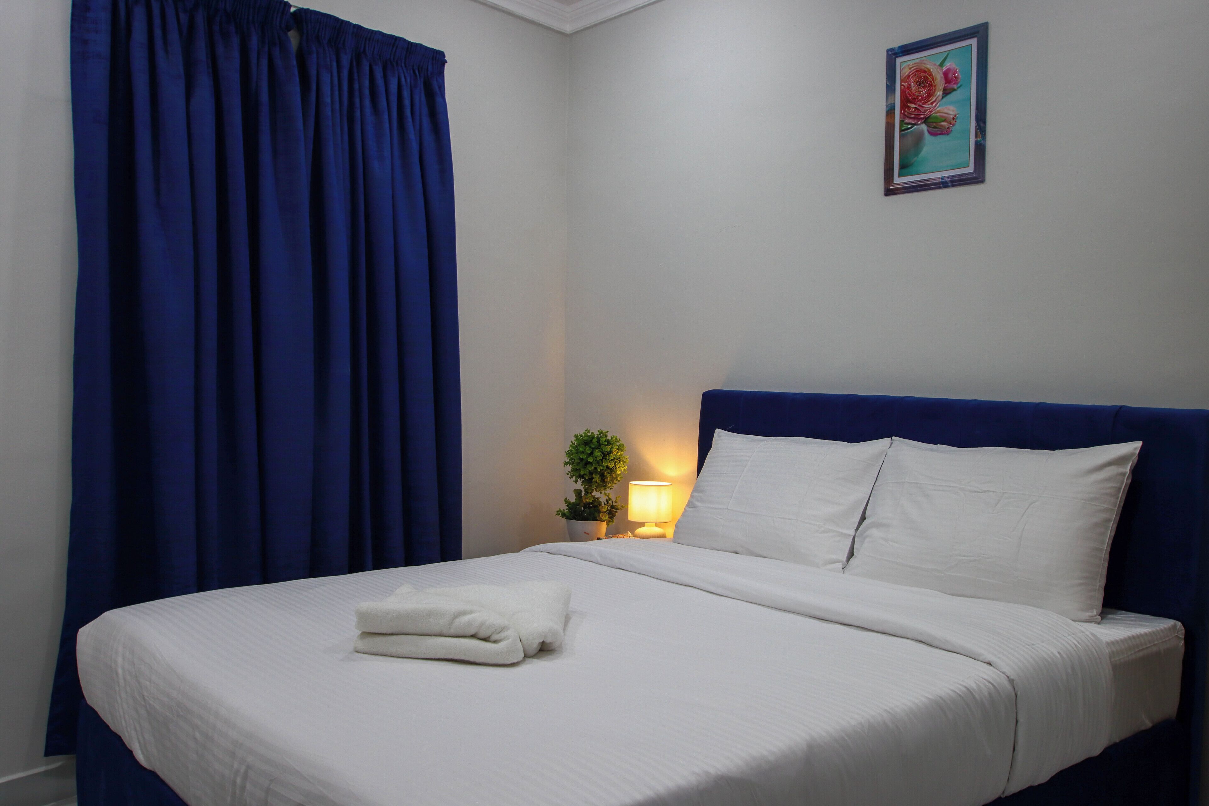 Ein ordentlich bezogenes Bett mit weißen Leinen und Kissen, ein blauer Kopfteil, ein Blumentopf und ein gerahmtes Bild an der Wand.