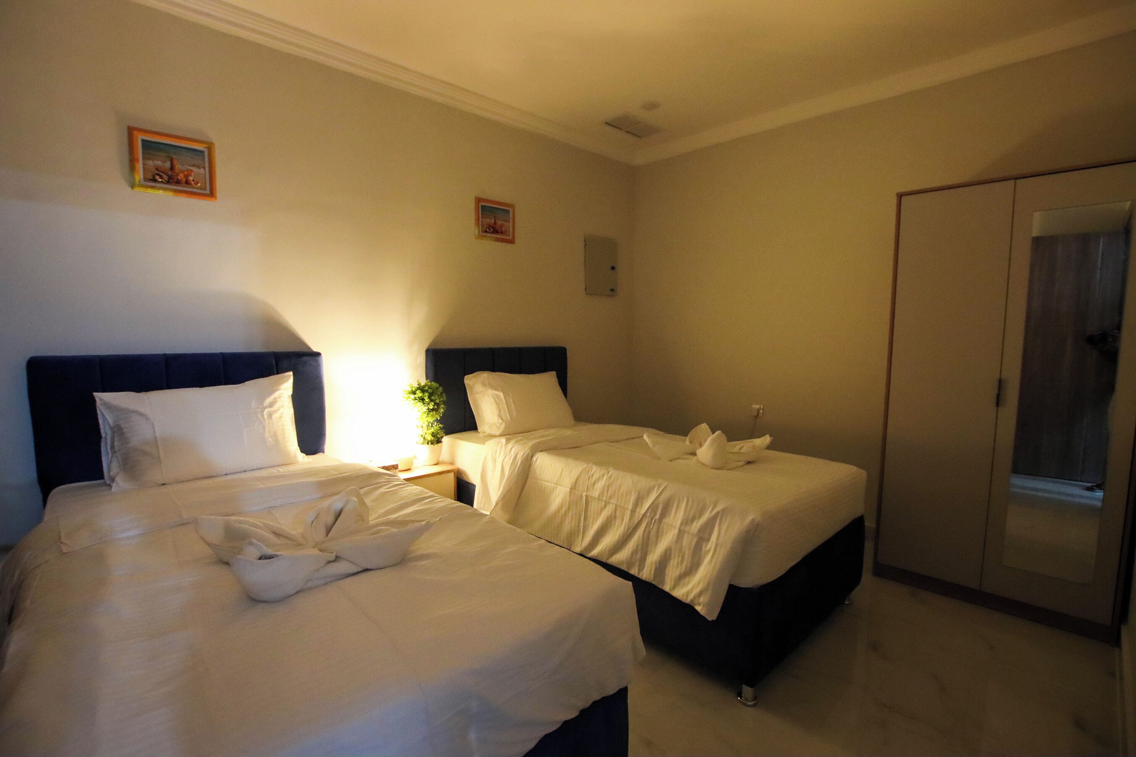 Habitación de hotel con dos camas, un armario y una pequeña mesa con una planta.