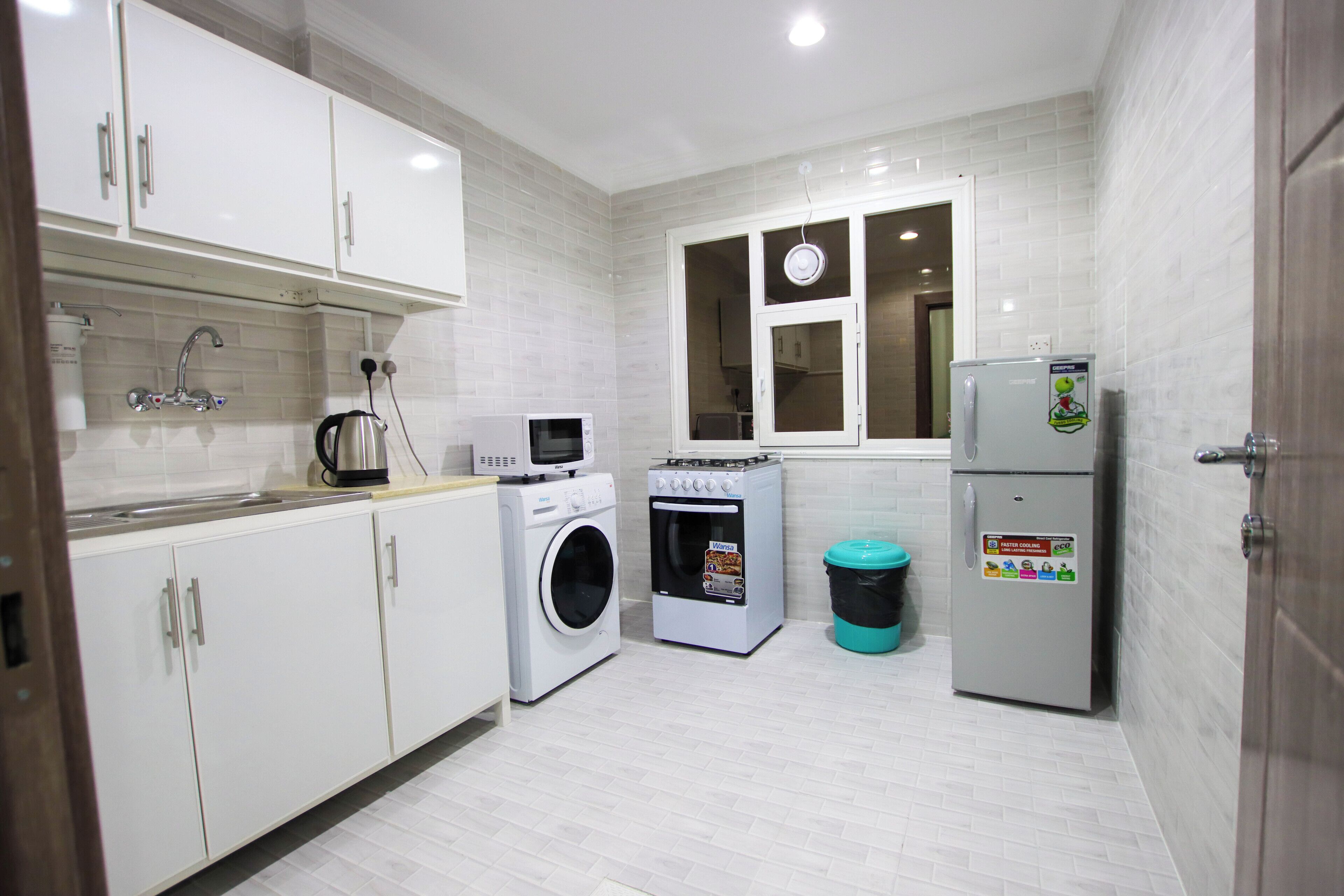 A compact kitchen with white cabinets, a washing machine, a microwave, and a refrigerator.
