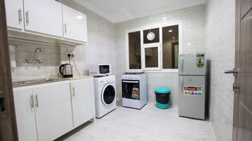 A compact kitchen with white cabinets, a washing machine, a microwave, and a refrigerator.