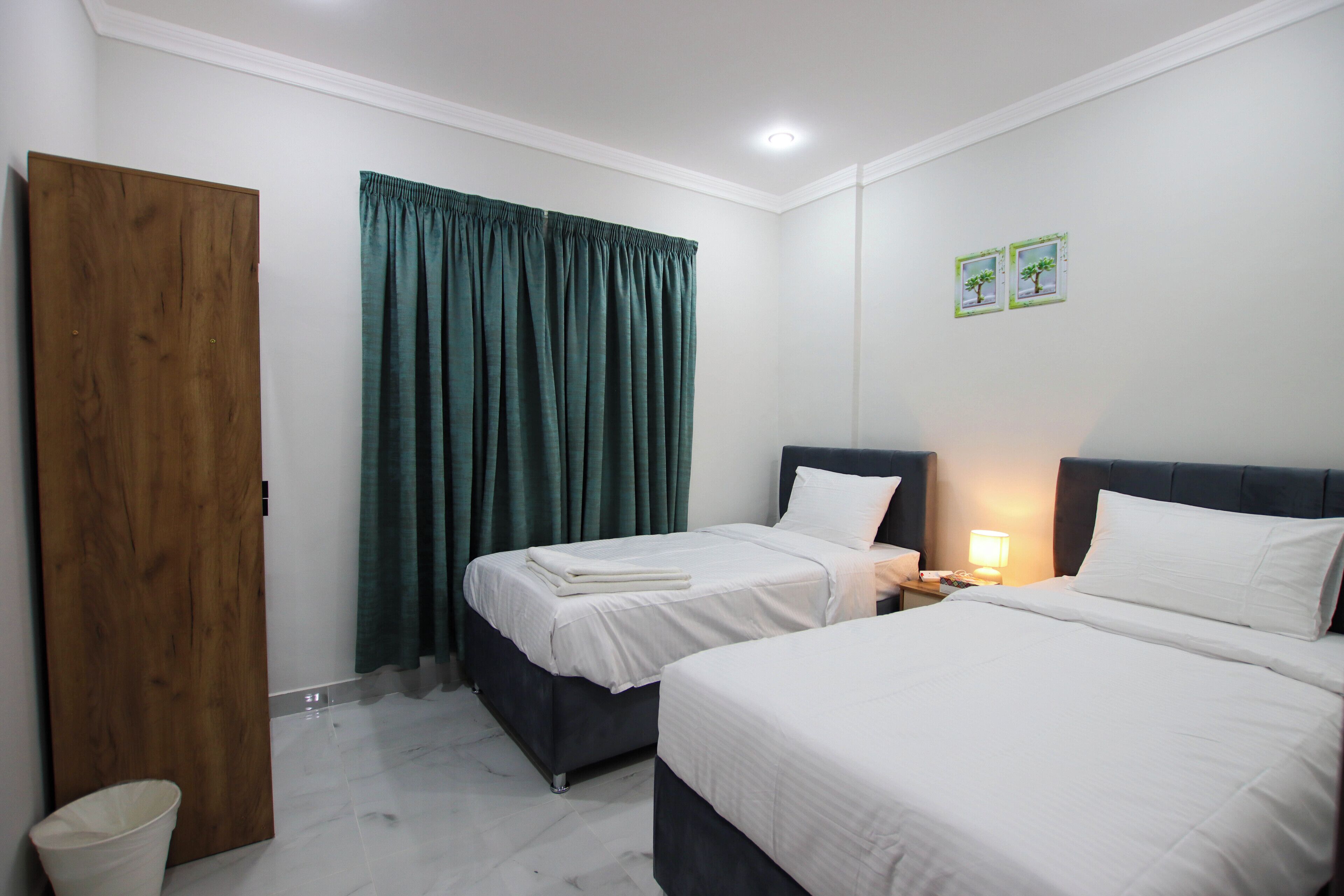 Een hotelkamer met twee bedden, een houten deur, een groen gordijn en een nachtkastje met een lamp.