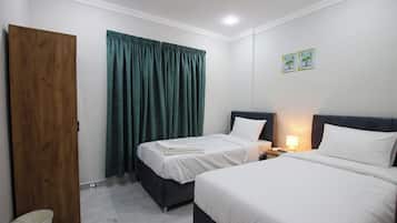 Een hotelkamer met twee bedden, een houten deur, een groen gordijn en een nachtkastje met een lamp.