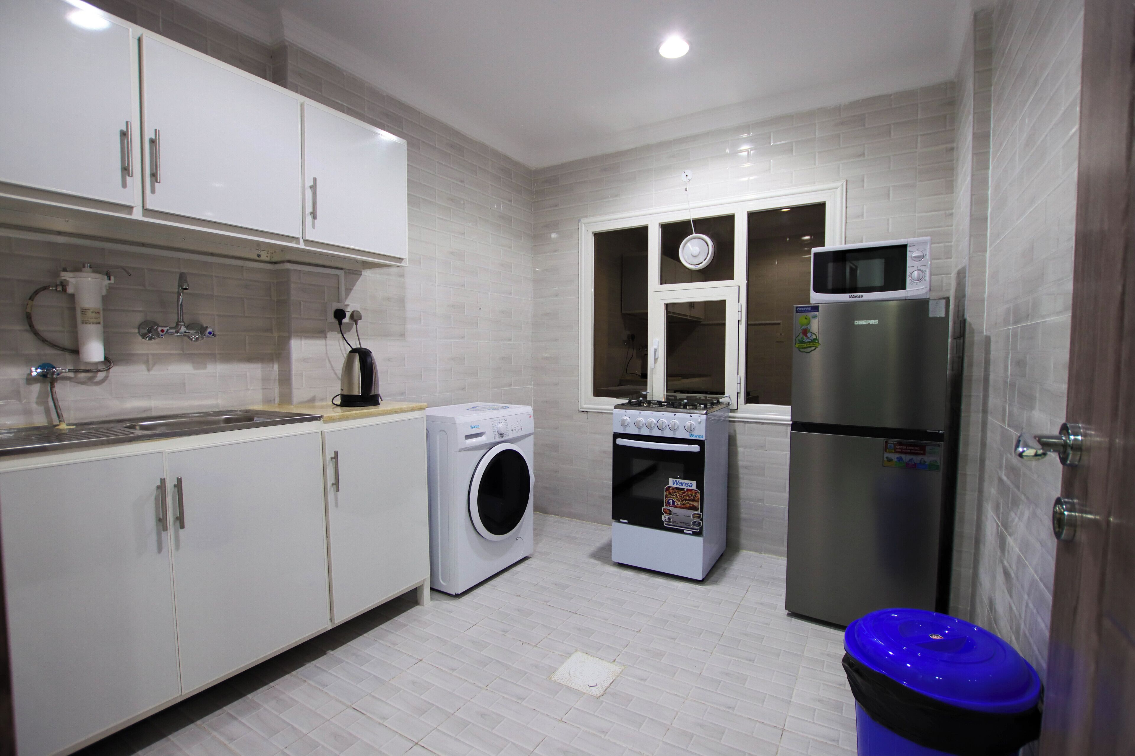 Een compacte keuken met witte kasten, een wasmachine, een oven, een magnetron en een koelkast.
