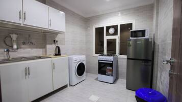 Een compacte keuken met witte kasten, een wasmachine, een oven, een magnetron en een koelkast.