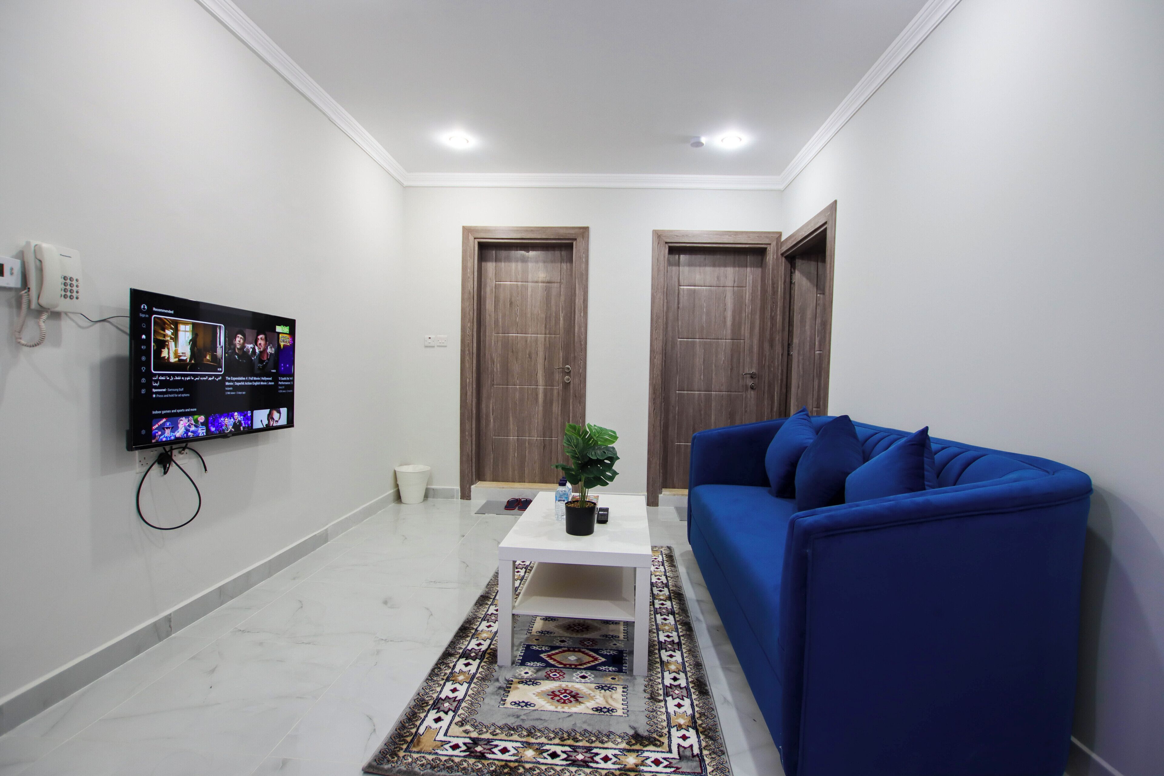 A living room with a blue sofa, a white coffee table, a TV mounted on the wall, and two wooden doors.