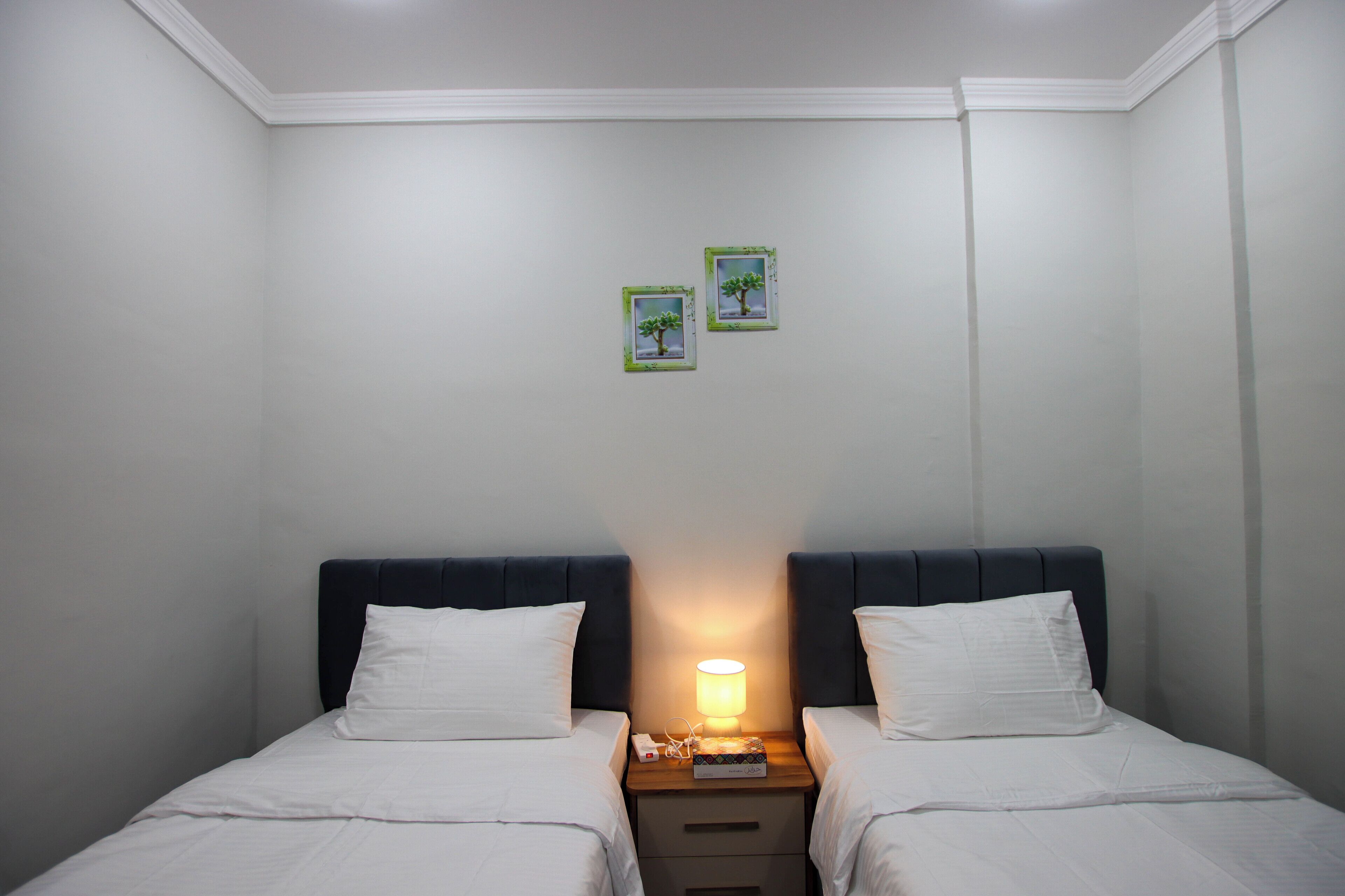 A double bed with white bedding, a nightstand with a lamp, and two framed pictures on the wall.