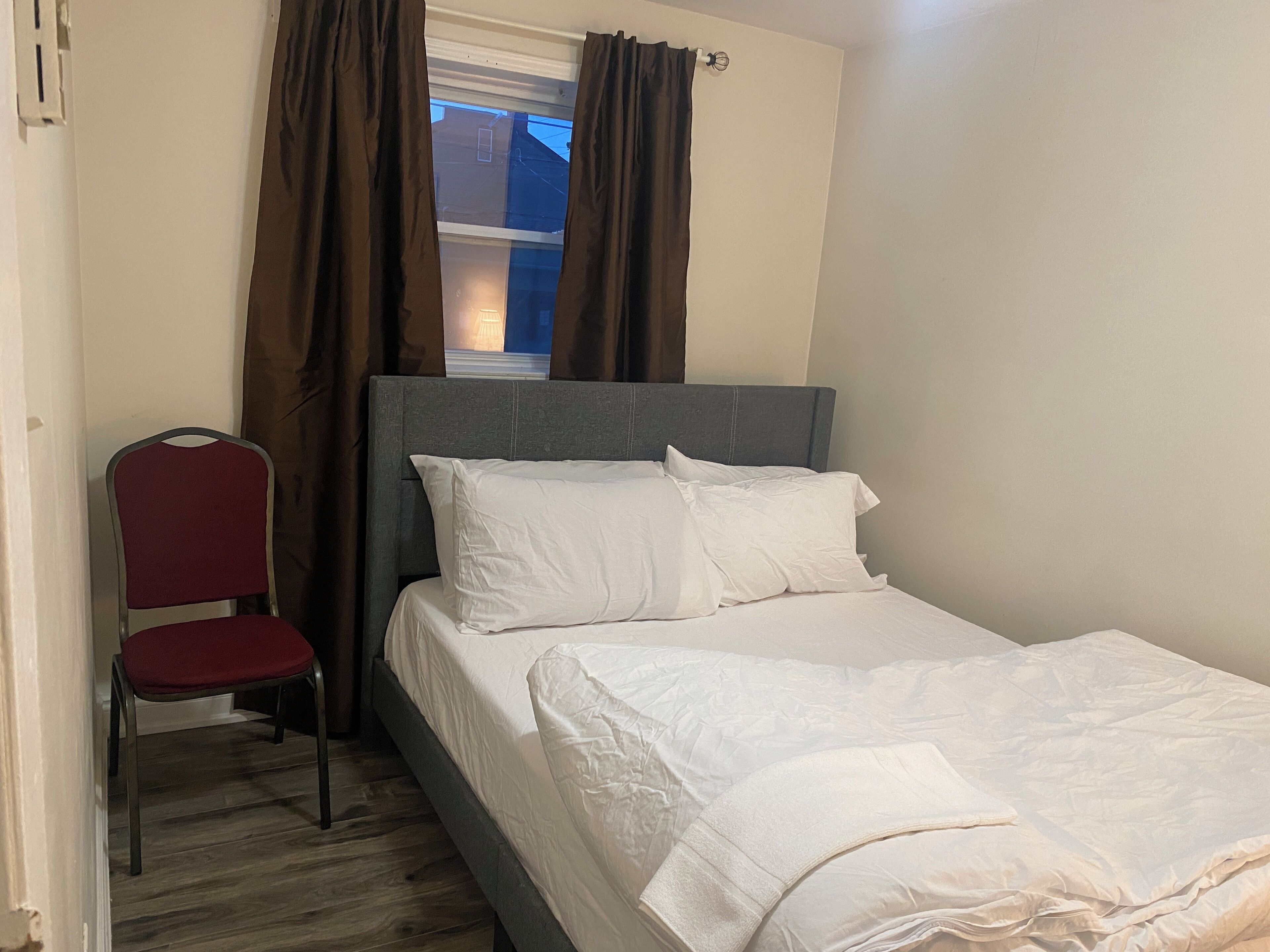 Un dormitorio pequeño con una cama individual, una silla y una ventana con cortinas.