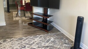 A living room with a flat-screen TV on a wooden stand, a dining area with red chairs, and a patterned rug on the floor. - Downtown Apartment 6 or 7 People (Bowmanville)