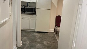A narrow hallway with a black mat at the entrance, leading to a kitchen area with white cabinets, a microwave, and a refrigerator. - Downtown Apartment 6 or 7 People (Bowmanville)