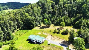A house with a green roof, surrounded by a forested area and a small clearing. - “Paradise Hill”  A Charming 3-bedroom house in the country. (Victor)