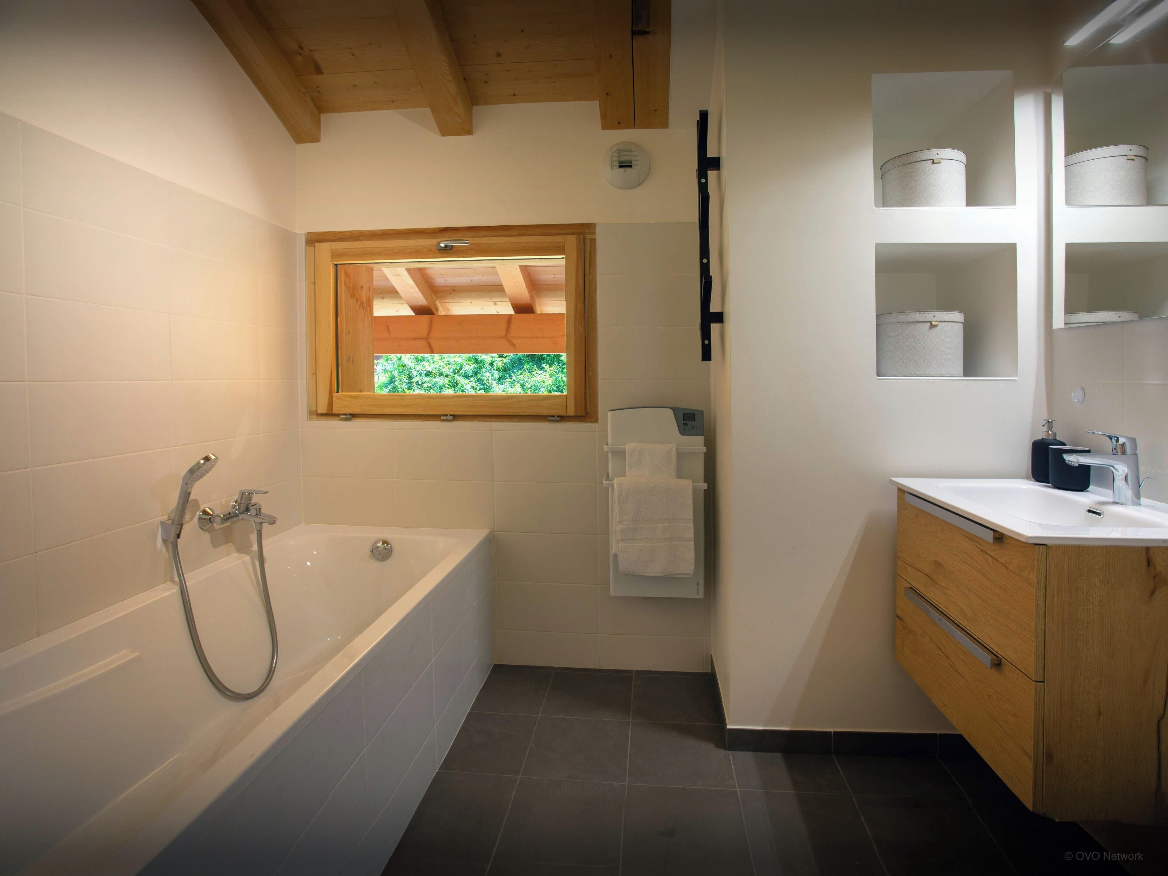 Un bagno moderno con vasca, una finestra vista verde, un water e un lavabo con pensili.