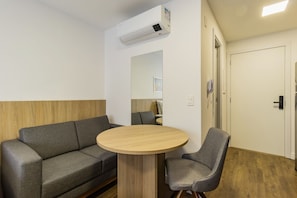 A room with a sofa, a round table, a chair, a mirror, a phone, and an air conditioning unit.