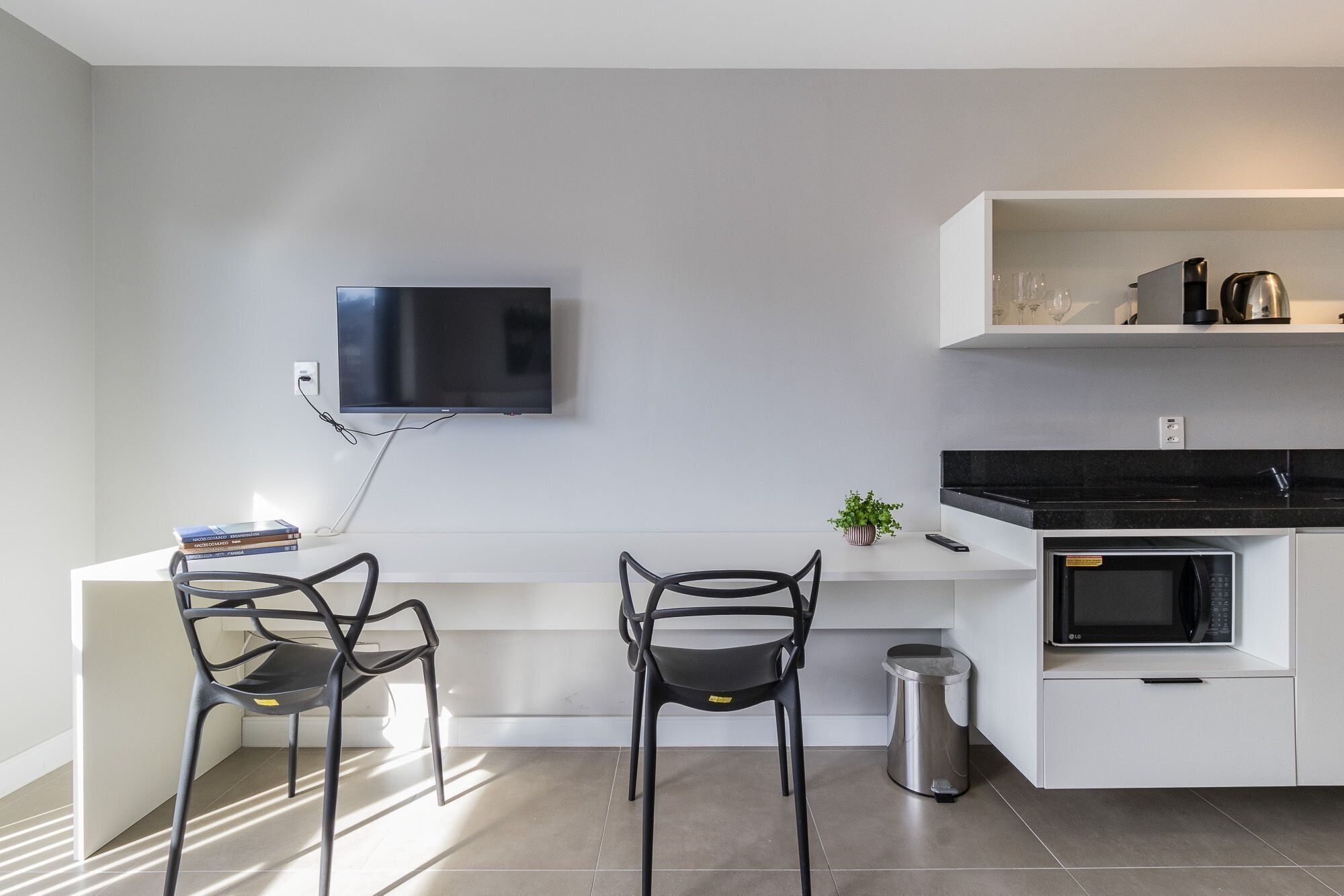 A modern kitchen with a flat-screen TV, two chairs, a small plant, and a microwave.