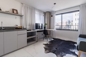 A modern kitchen with a dining area, a large window with a city view, and a unique black and white rug.