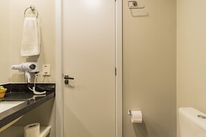 A bathroom with a white toilet, a towel hanging on a ring, a hair dryer on the counter, and a toilet paper holder.