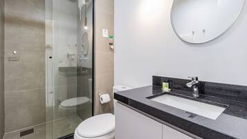 A modern bathroom with a glass shower enclosure, a white toilet, a sink with a black countertop, and a round mirror.