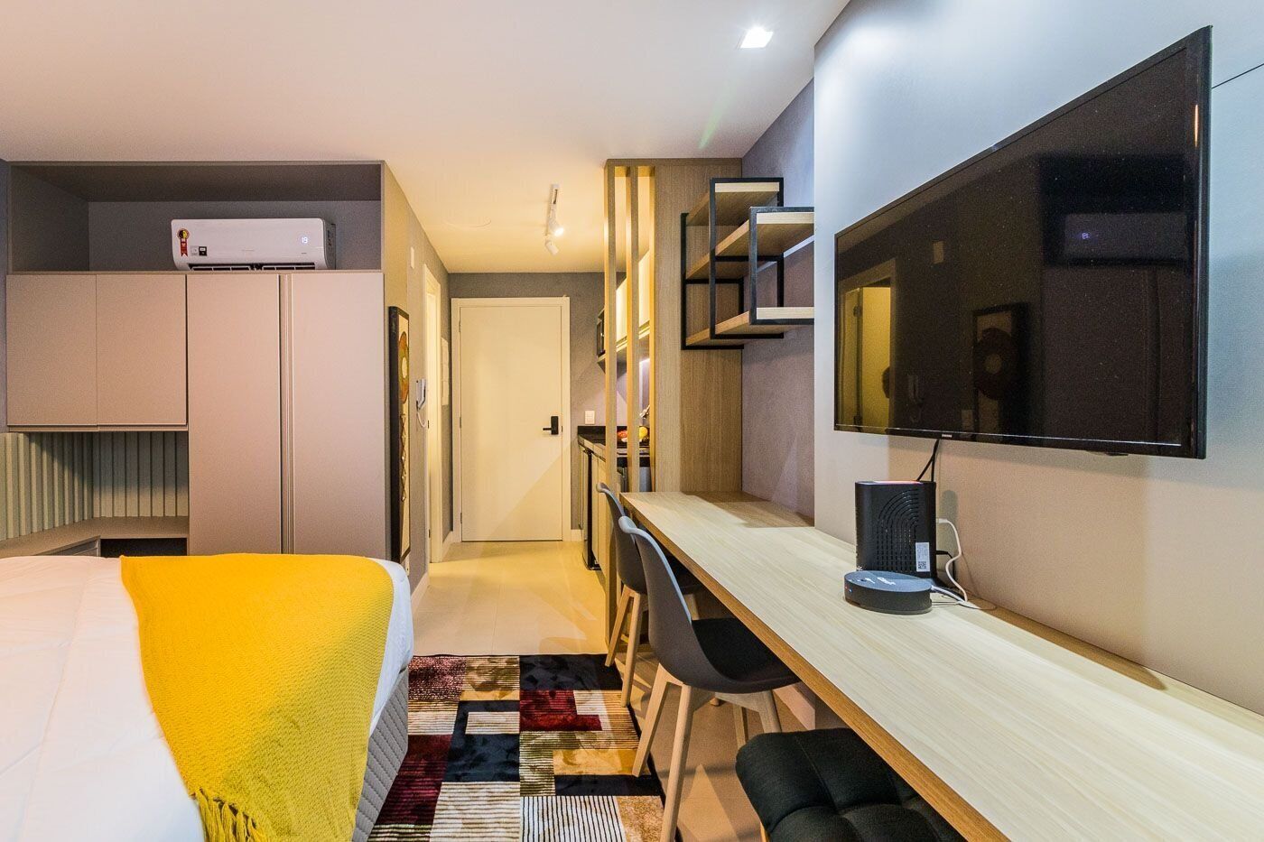 Una camera d'albergo moderna con un letto, una scrivania, una sedia, una TV e un condizionatore d'aria integrato.