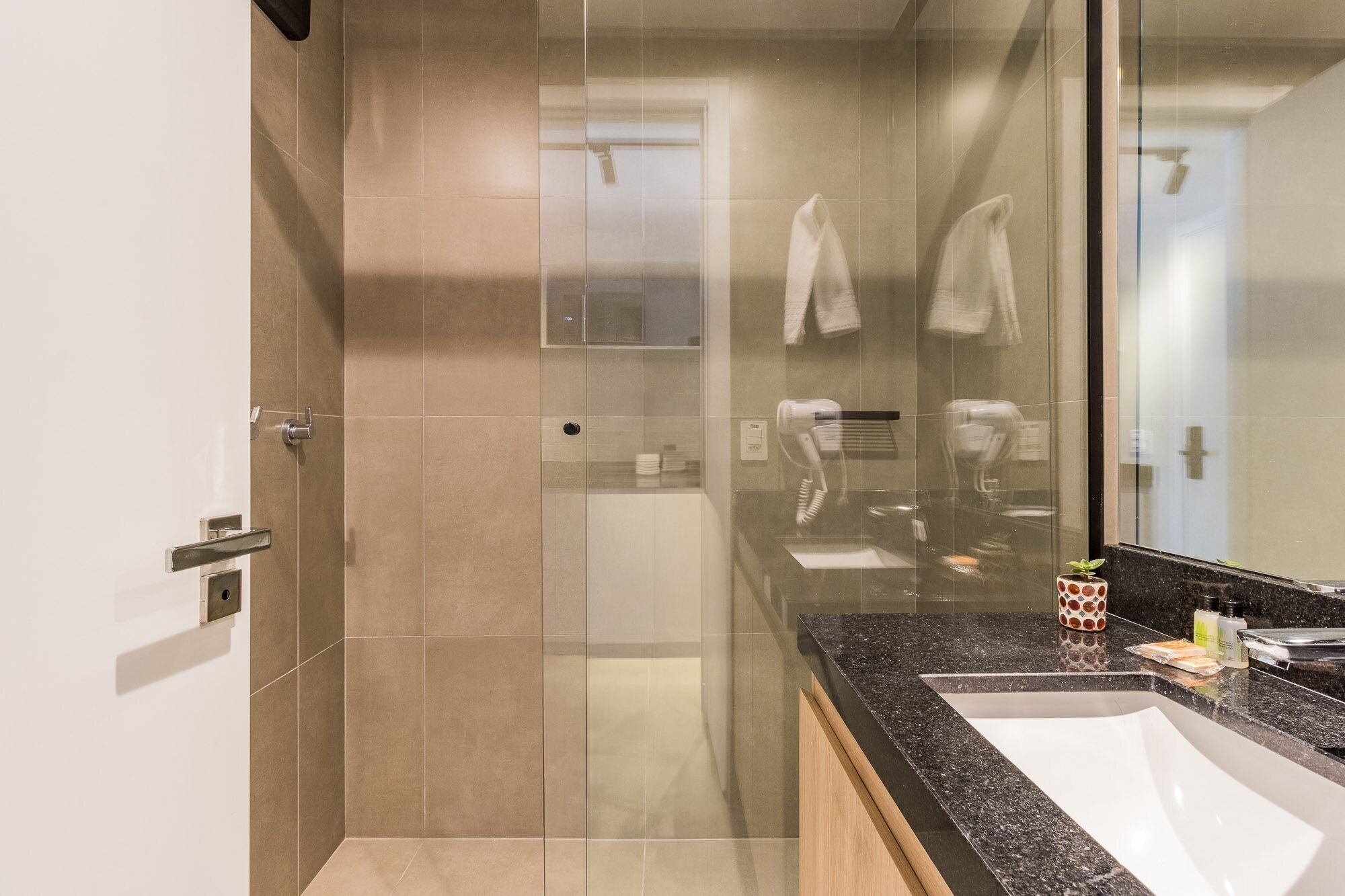 Un baño moderno con cabina de ducha de vidrio, un lavamanos con encimera de granito y un espejo que refleja el interior.