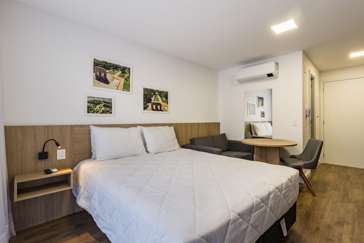 Habitación de hotel con cama, escritorio, silla y una mesita. Hay tres cuadros en la pared.
