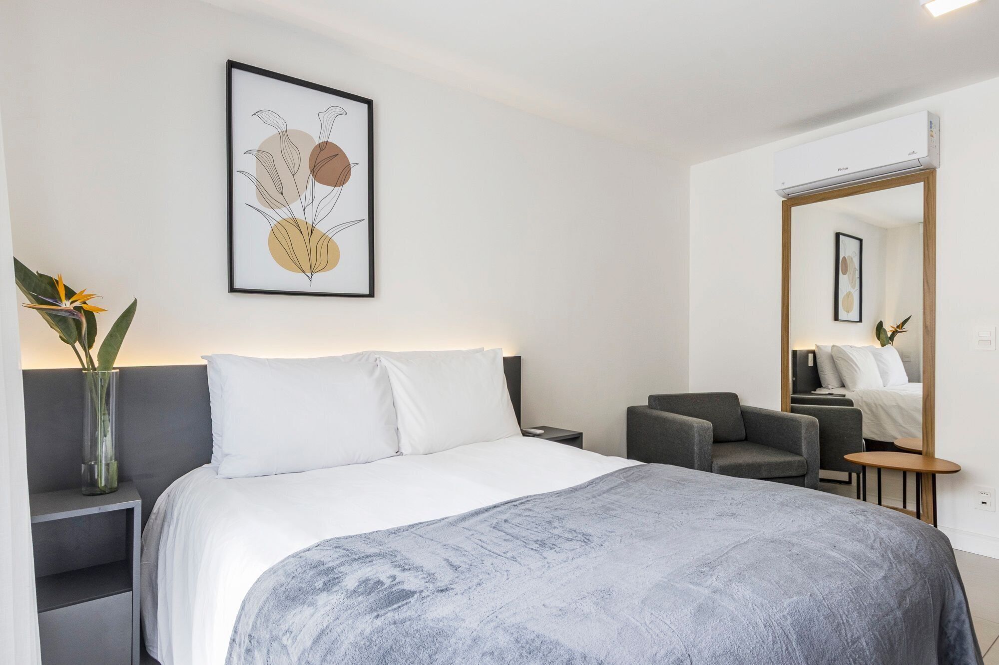 Ein modernes Hotelzimmer mit Bett, Nachttisch, Stuhl und einem großen Spiegel.