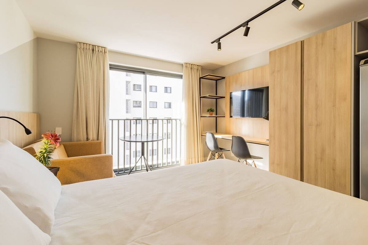Una habitación de hotel con una cama, un escritorio con dos sillas, un televisor y un balcón con cortinas.
