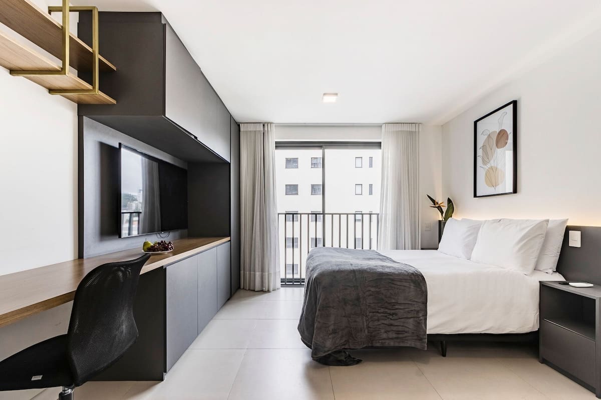 Habitación de hotel moderna con cama, mesita de noche, escritorio, silla y vista a la ciudad por la ventana.
