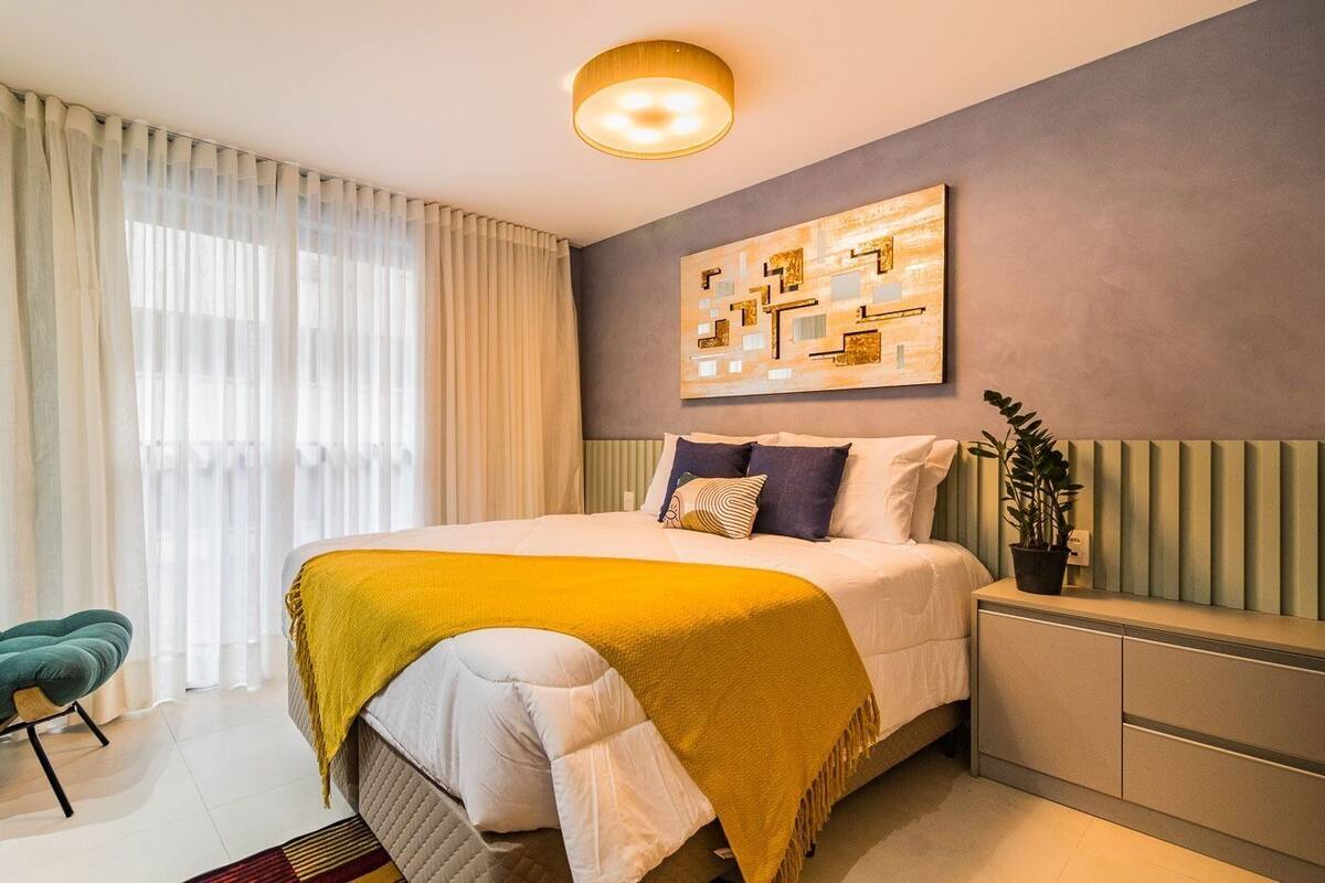 Un dormitorio moderno con cama, mesita de noche, planta en maceta y un cuadro en la pared.