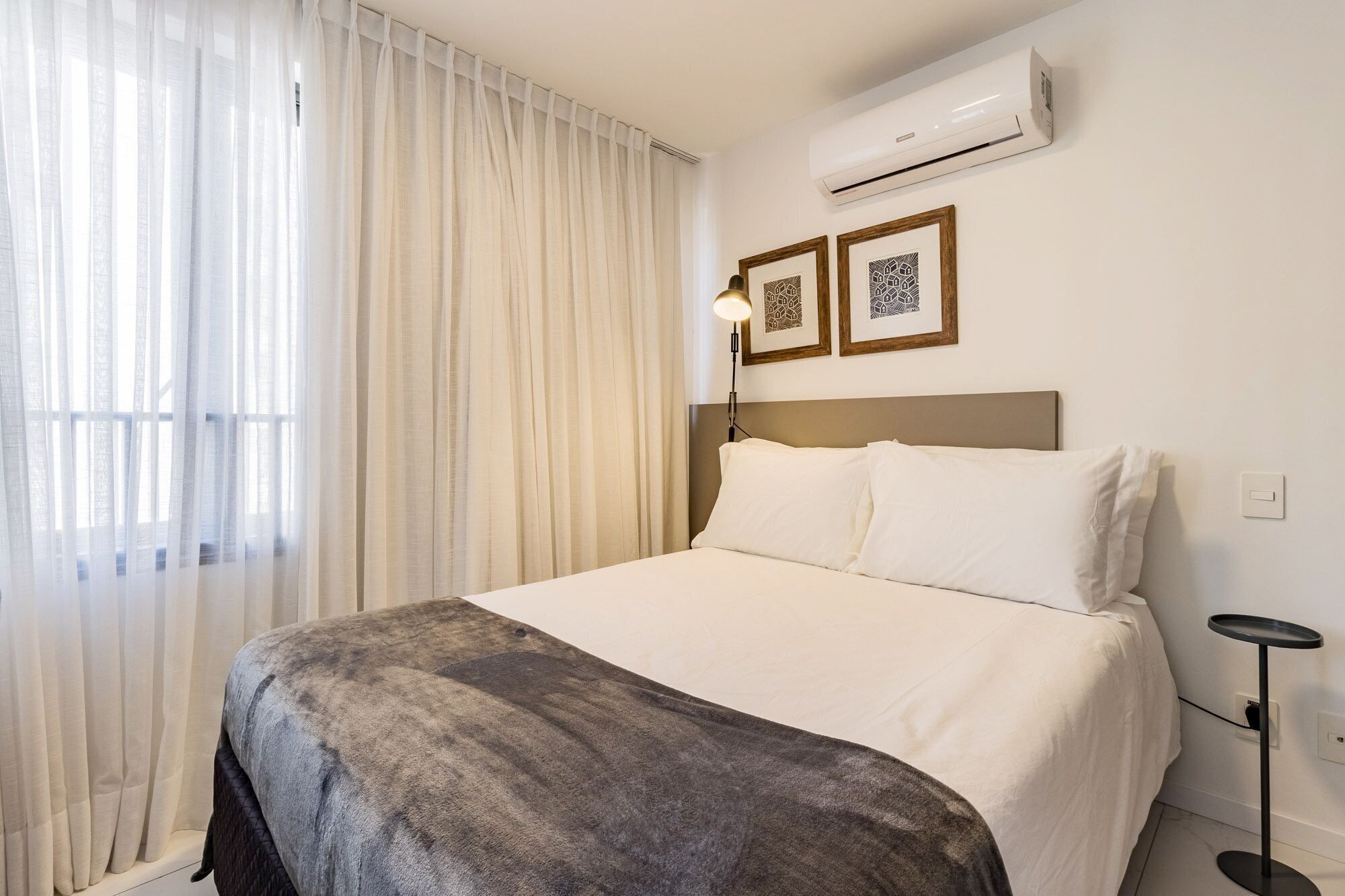 Ein Hotelzimmer mit Bett, Klimaanlage, Lampe und zwei gerahmten Bildern an der Wand.