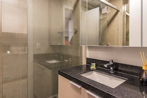 A modern bathroom with a glass shower enclosure, a sink with a black countertop, and a mirror above the sink.