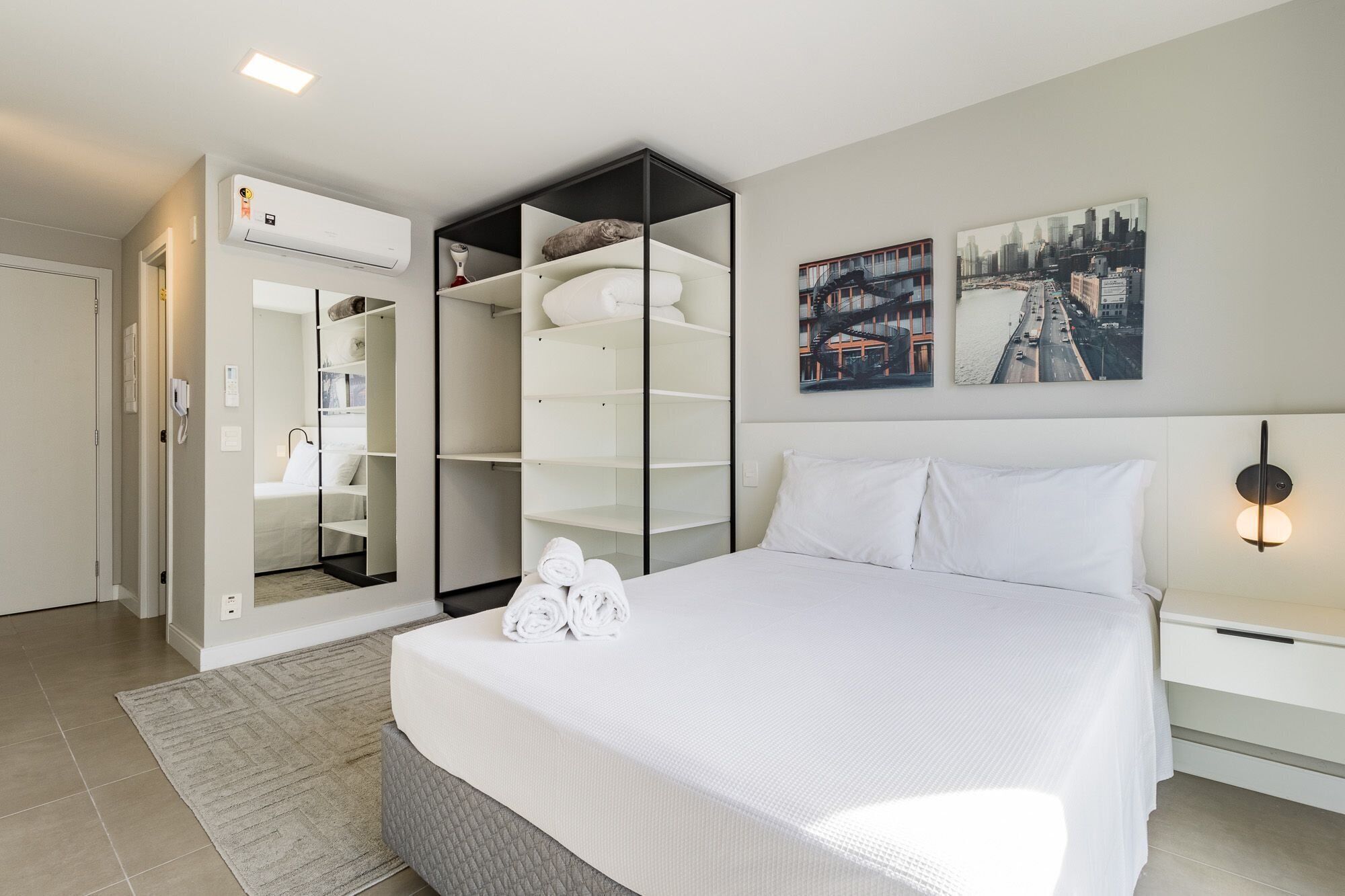 Ein Hotelzimmer mit einem Bett, einem Einbauschrank, einer Wand-Klimaanlage und zwei Stadtbildern.