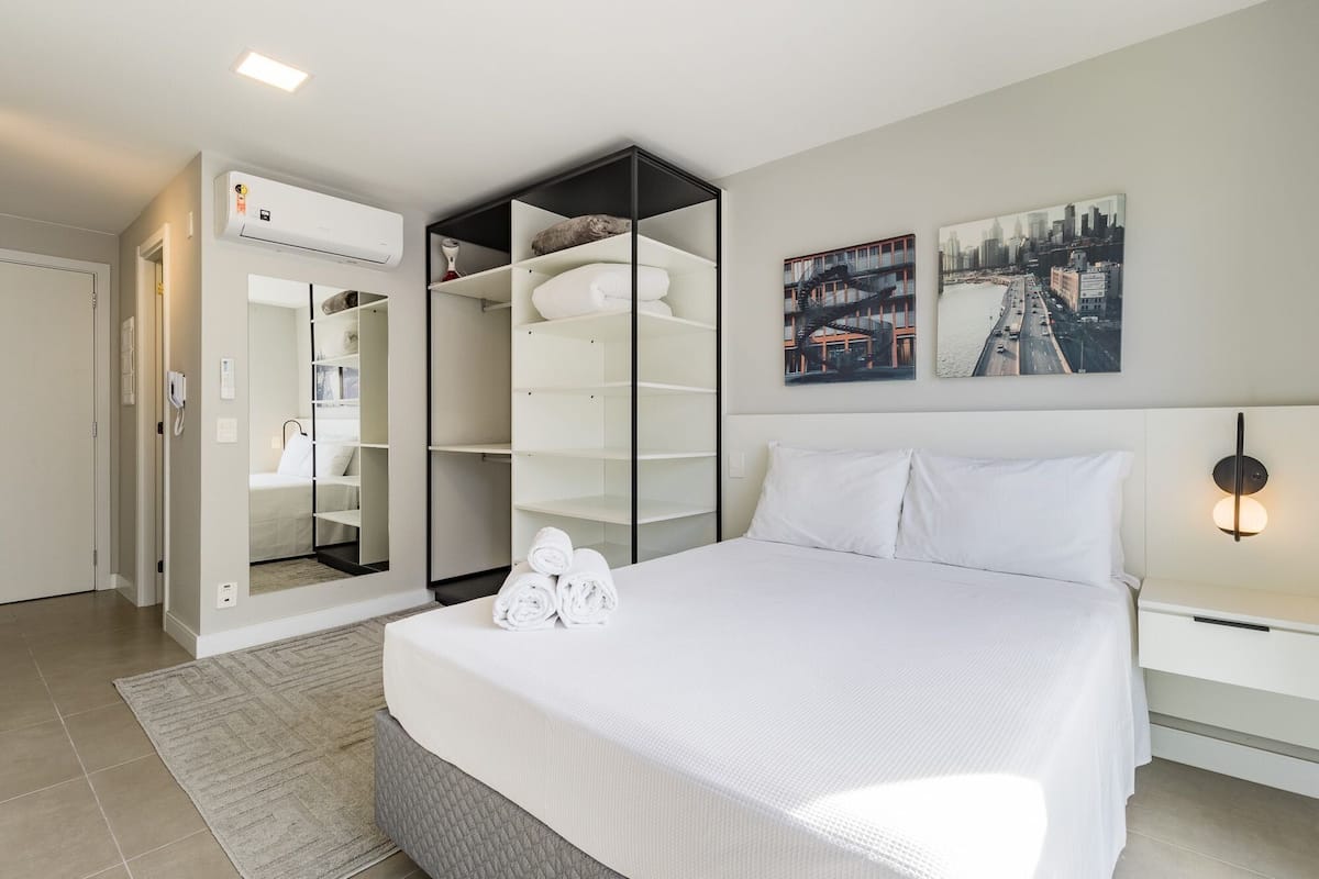 Habitación de hotel con cama, armario empotrado, aire acondicionado de pared y dos cuadros con vistas a la ciudad.