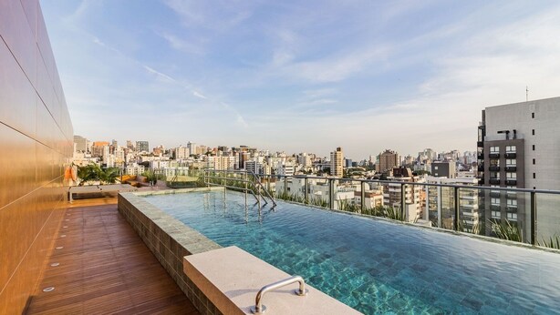 A rooftop infinity pool with a city view, wooden deck, and metal railings. - Go 24 By My Way (Porto Alegre)