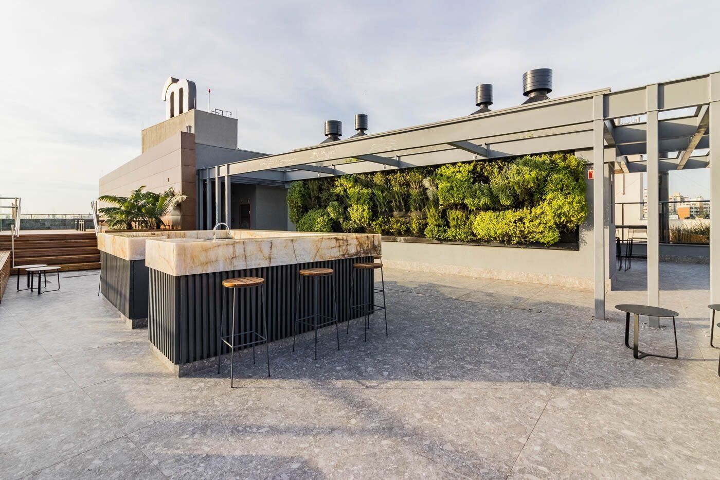 A rooftop bar with a marble counter, bar stools, and a pergola structure.