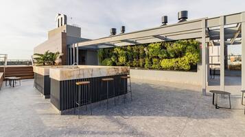 A rooftop bar with a marble counter, bar stools, and a pergola structure.