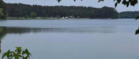 A calm lake with a forested shoreline and a few buildings in the distance.