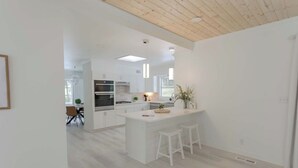 Una cocina moderna con armarios blancos, una isla central con taburetes y un comedor al fondo.