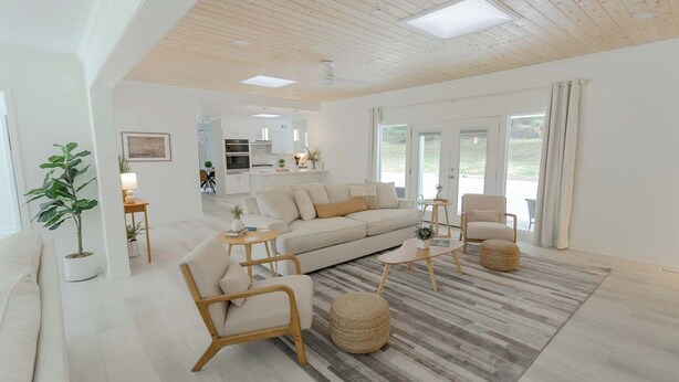 Un salón espacioso con sofá, sillones y una mesa de centro. Se ve una cocina al fondo, y un ventanal grande ofrece luz natural.