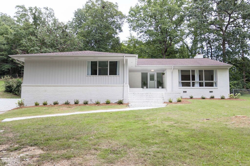 A single-story house with a front porch, a small front yard, and a wooded backdrop.