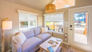 A cozy living room with a sofa, a coffee table, and a door leading to an outdoor deck. - Rainforest Tiny Home Retreat: Coastal (Forks)