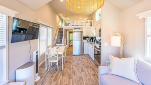 A modern kitchen with a dining area, wooden flooring, and a staircase leading to an upper level. - Rainforest Tiny Home Retreat: Coastal (Forks)