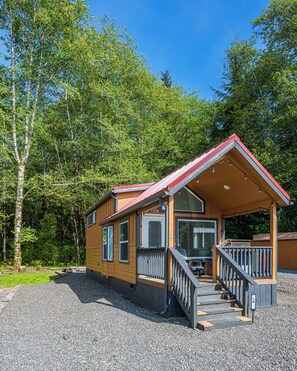 A wooden cabin with a porch, a staircase, and a gravel driveway. - Rainforest Tiny Home Retreat: Coastal (Forks)