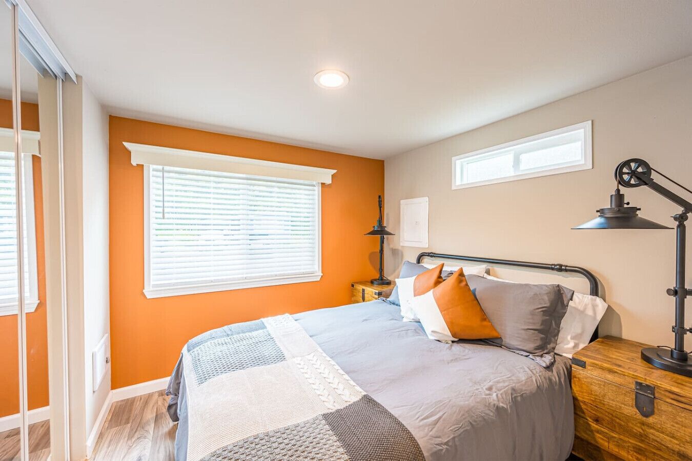 A bedroom with a bed, a nightstand, a lamp, and a window with blinds.