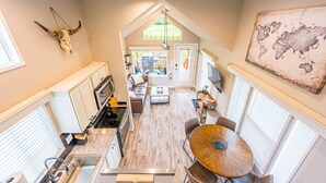 A modern kitchen with a central island, a dining area with a round table, and a living space with a sofa and TV. - Rainforest Tiny Home Retreat: Industrial (Forks)