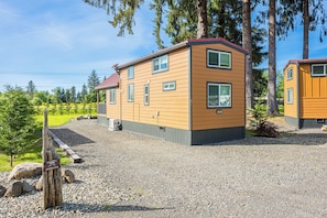 A cabin with a sloped roof, multiple windows, and a gravel driveway. - Rainforest Tiny Home Retreat: Industrial (Forks)