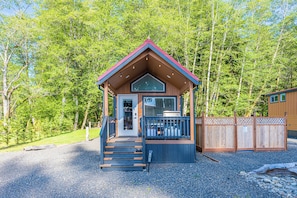 A cabin with a wooden exterior, a porch, and a gravel driveway.