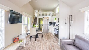 Eine moderne Küche mit einer zentralen Kochinsel, ein Essbereich mit Tisch und Stühlen, ein Wohnzimmer mit Sofa und eine Treppe, die in ein Obergeschoss führt.